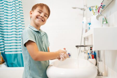 Atividades sobre Higiene Pessoal: Ideias e modelos em PDF menino sorridente pre escolar lavando as maos com sabao debaixo da torneira com agua scaled e1680649058105