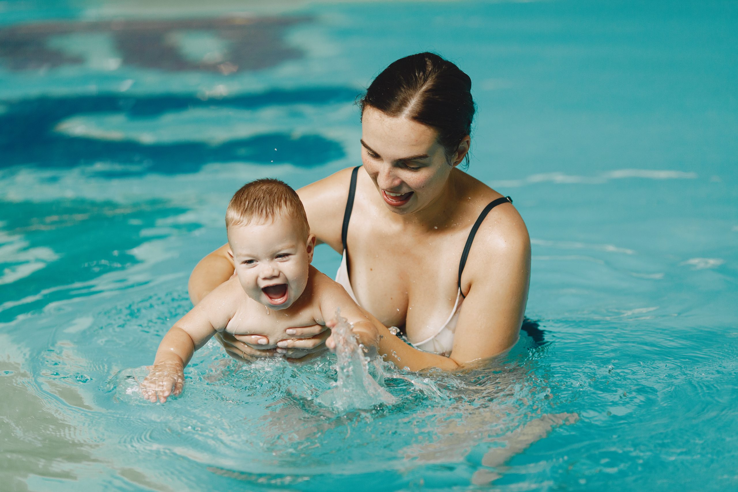 Mulher segura bebê em piscina enquanto ele bate as mãos na água