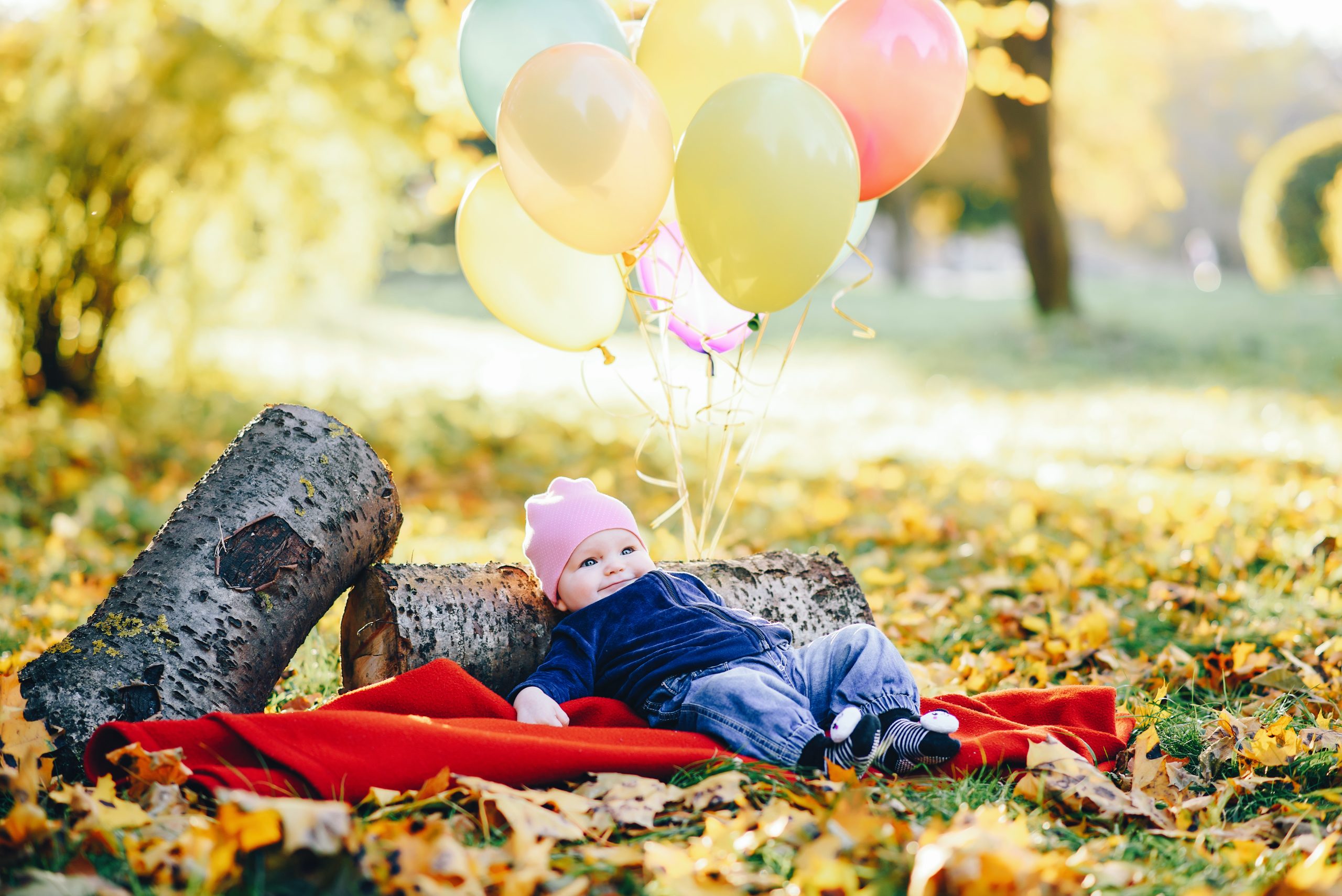 Bebê deitado de barriga pra cima em um parque observa balões flutuando acima de si
