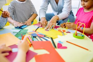 Professora com três alunos fazendo atividade de recorte e pintura