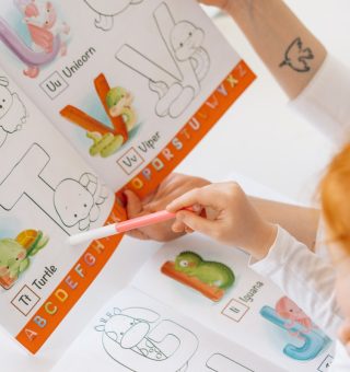 Criança acompanhando a professora indicando um banner colorida com letras do alfabeto e ilustrações