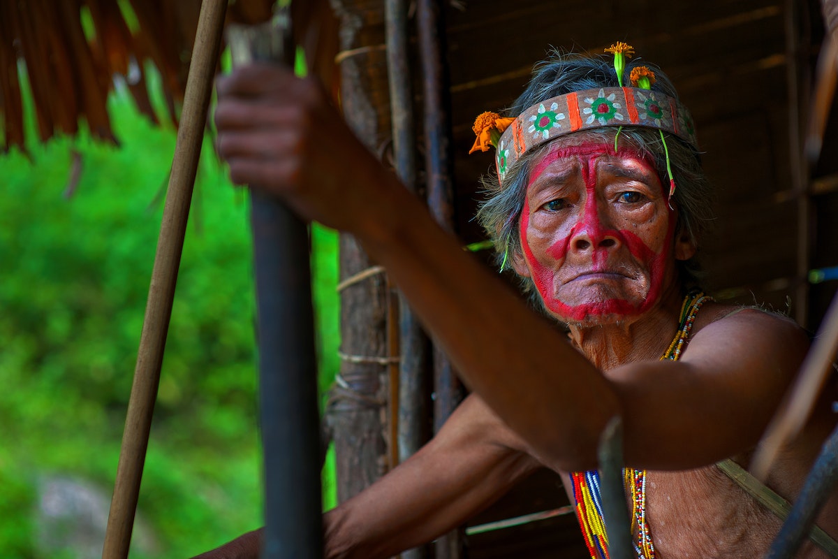 Foto de um índio sentado com o rosto pintado parcialmente de vermelho 