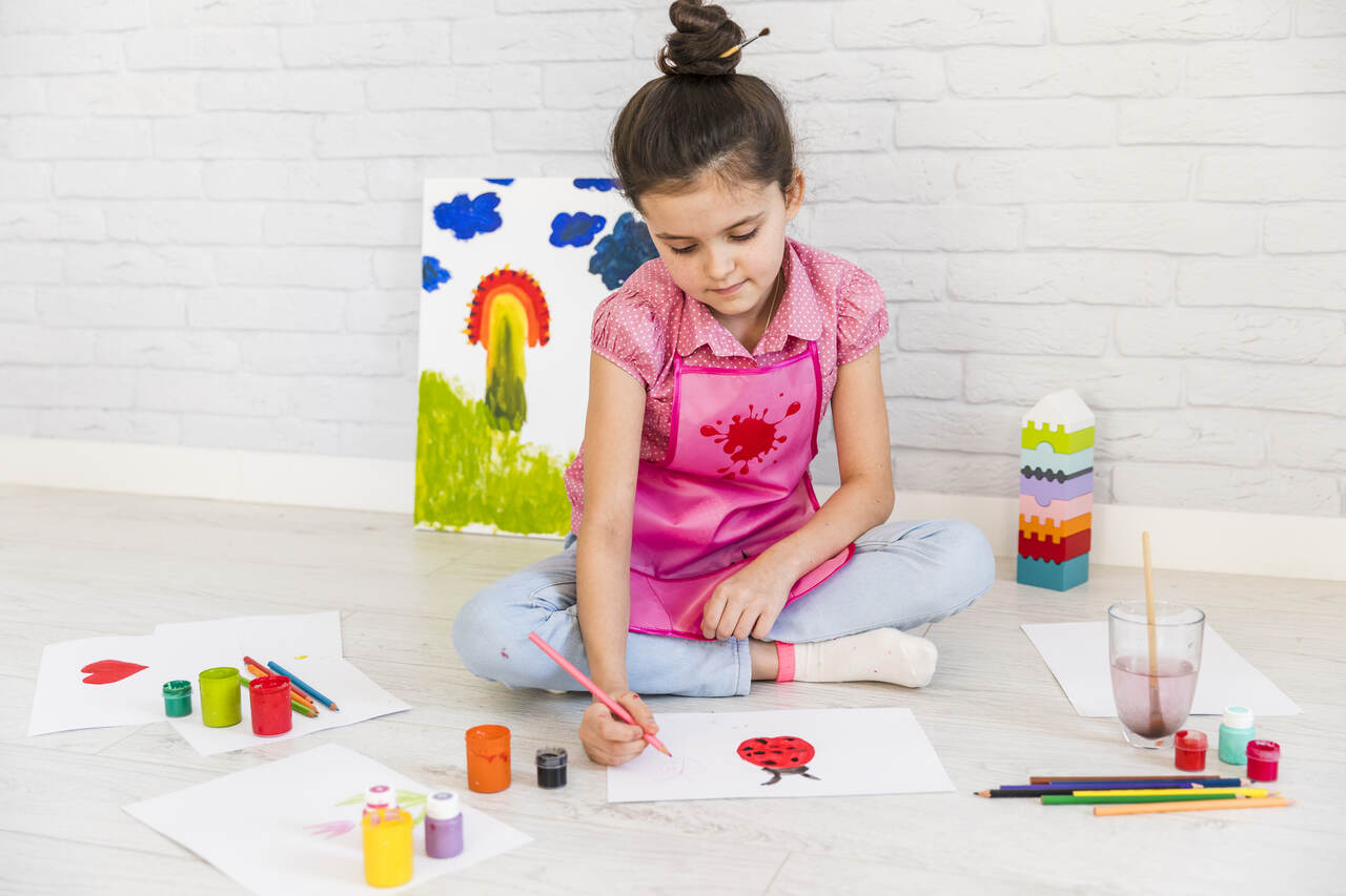 Menina sentada fazendo atividade com tinta guache para educação infantil