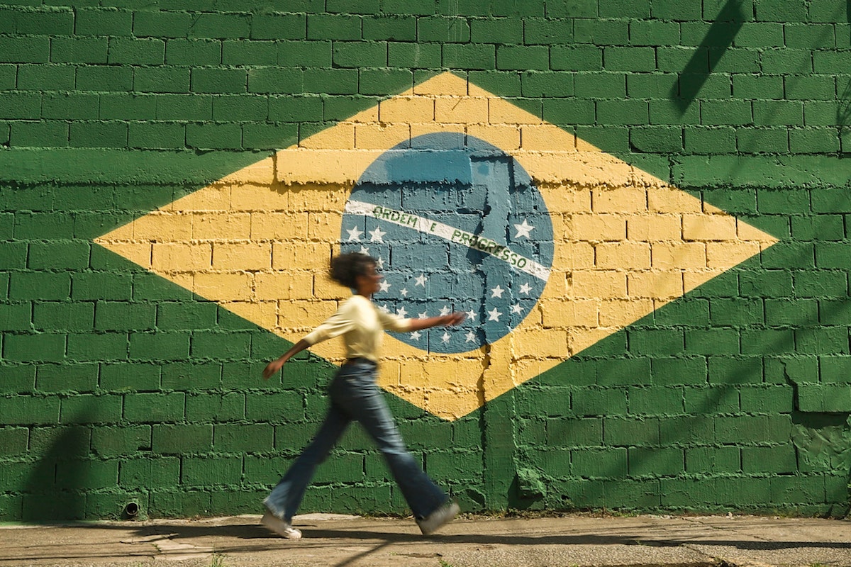 Uma mulher desfilando em frente a uma parede onde está pintada a bandeira do Brasil