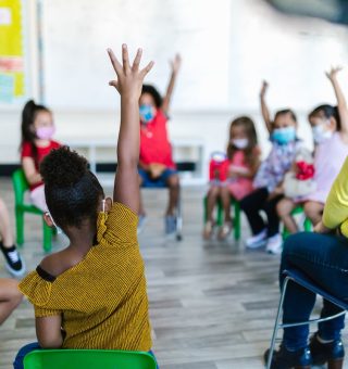 Turma de alunos [crianças] na sala de aula sentados e com um dos braços levantados