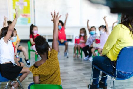 Turma de alunos [crianças] na sala de aula sentados e com um dos braços levantados