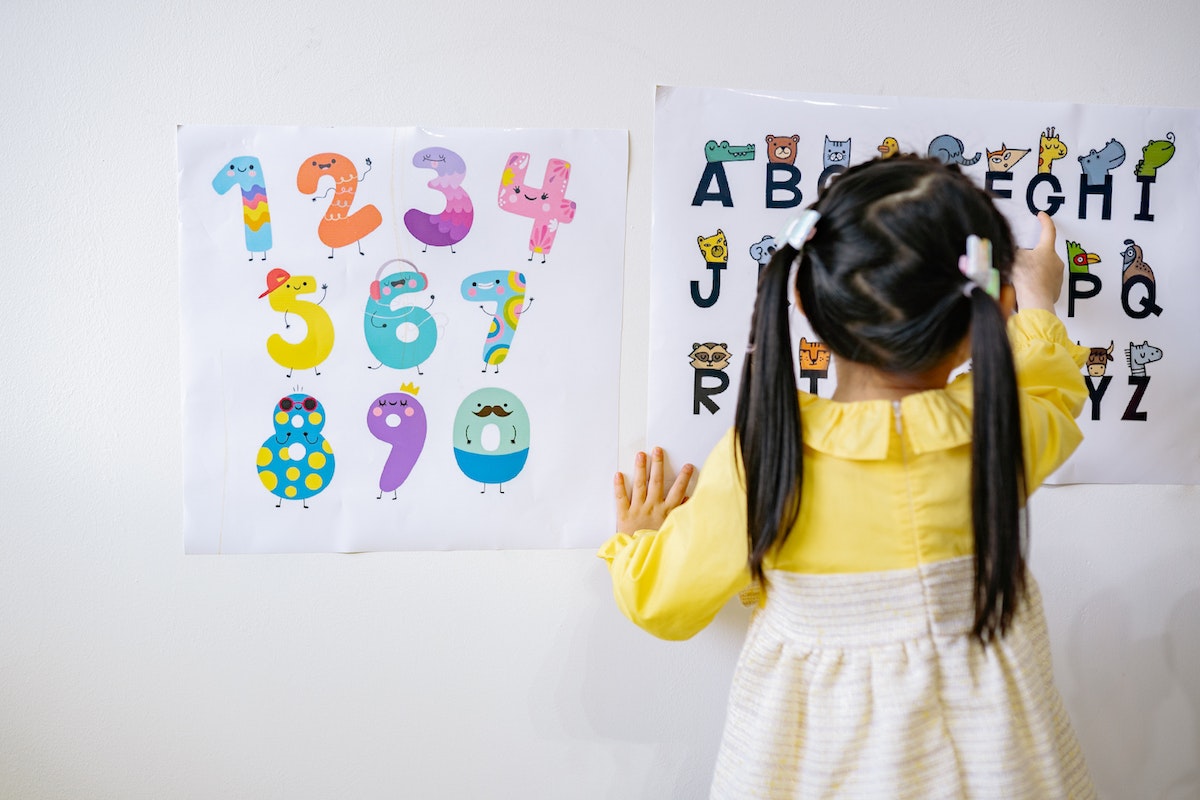 Aluna criança olhando para a parede onde tem o numeral de 1 a 10 e o alfabeto