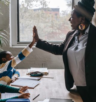 Professora negra tocando na mão de um de seus alunos, como em sinal de comemoração