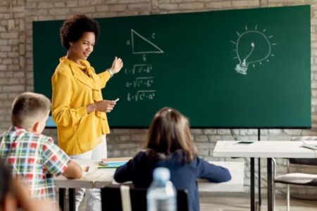 Uma professora na frente do quadro mostrando a atividade de matemática para os alunos