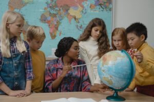Atividades para Imprimir para Criança de 9 Anos Professora mostrando para a sua turma um continente no globo terrestre em cima da mesa