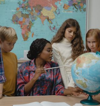 Professora mostrando para a sua turma um continente no globo terrestre em cima da mesa