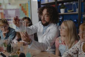 Professor dequímica faz experimento com alguns alunos que o acompanham sentados ao seu lado