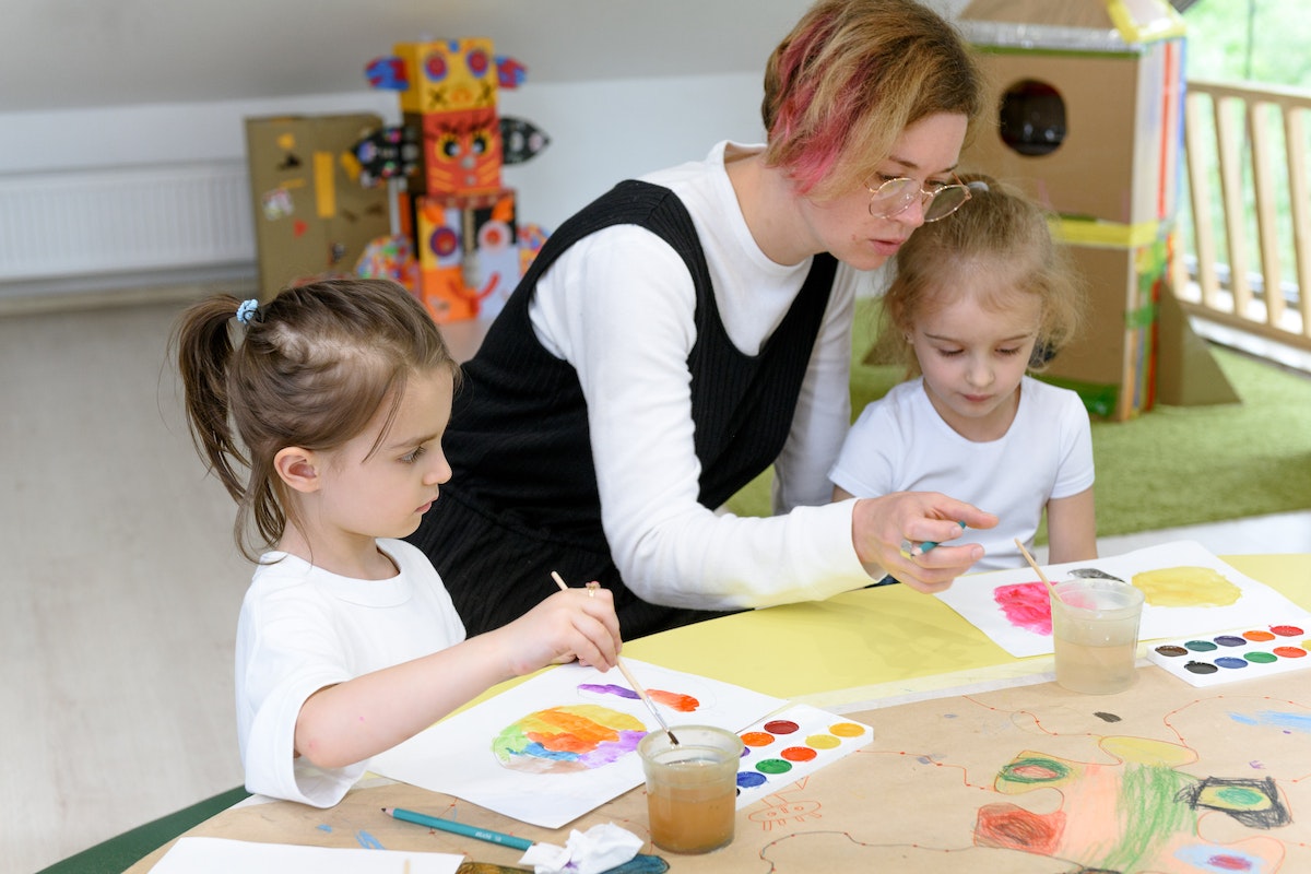Uma professora está ao lado de seus alunos durante uma aula de pintura