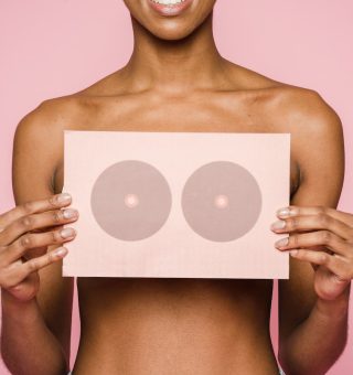 Uma mulher segura um papel em frente ao seu peito representando a luta pelo câncer de mama