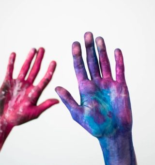 Duas mãos humanas estão cobertas de tintas.