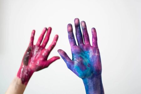 Duas mãos humanas estão cobertas de tintas.