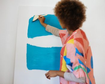 Uma professora está pintando a parede da sala com um pincel e tinta azul