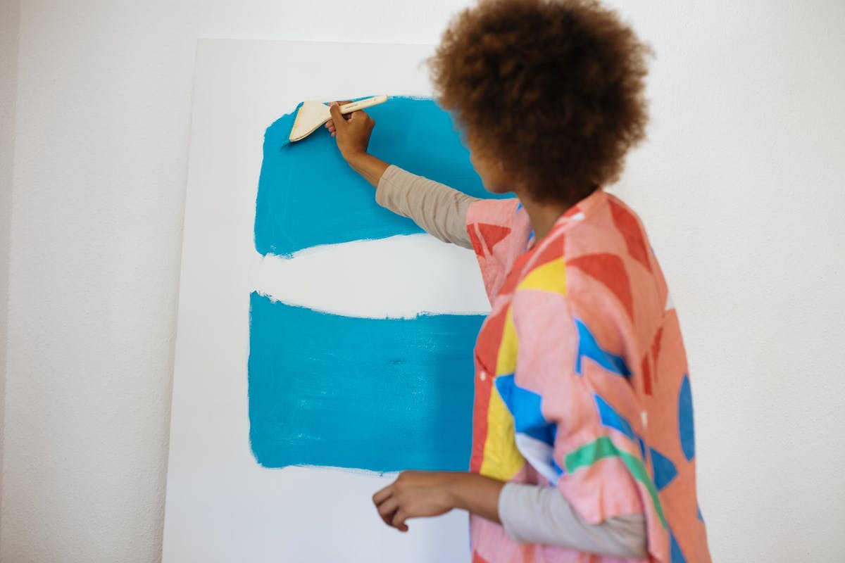 Uma professora está pintando a parede da sala com um pincel e tinta azul