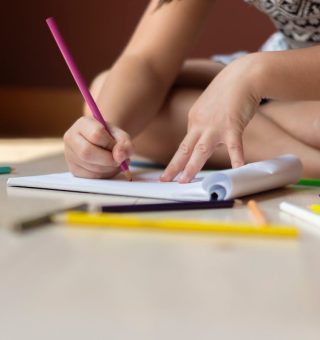 Uma menina está pintando em um caderno usando lápis de cor