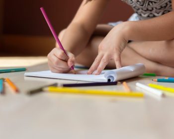 Uma menina está pintando em um caderno usando lápis de cor