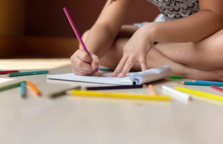 Uma menina está pintando em um caderno desenhos de natal para copiar usando lápis de cor