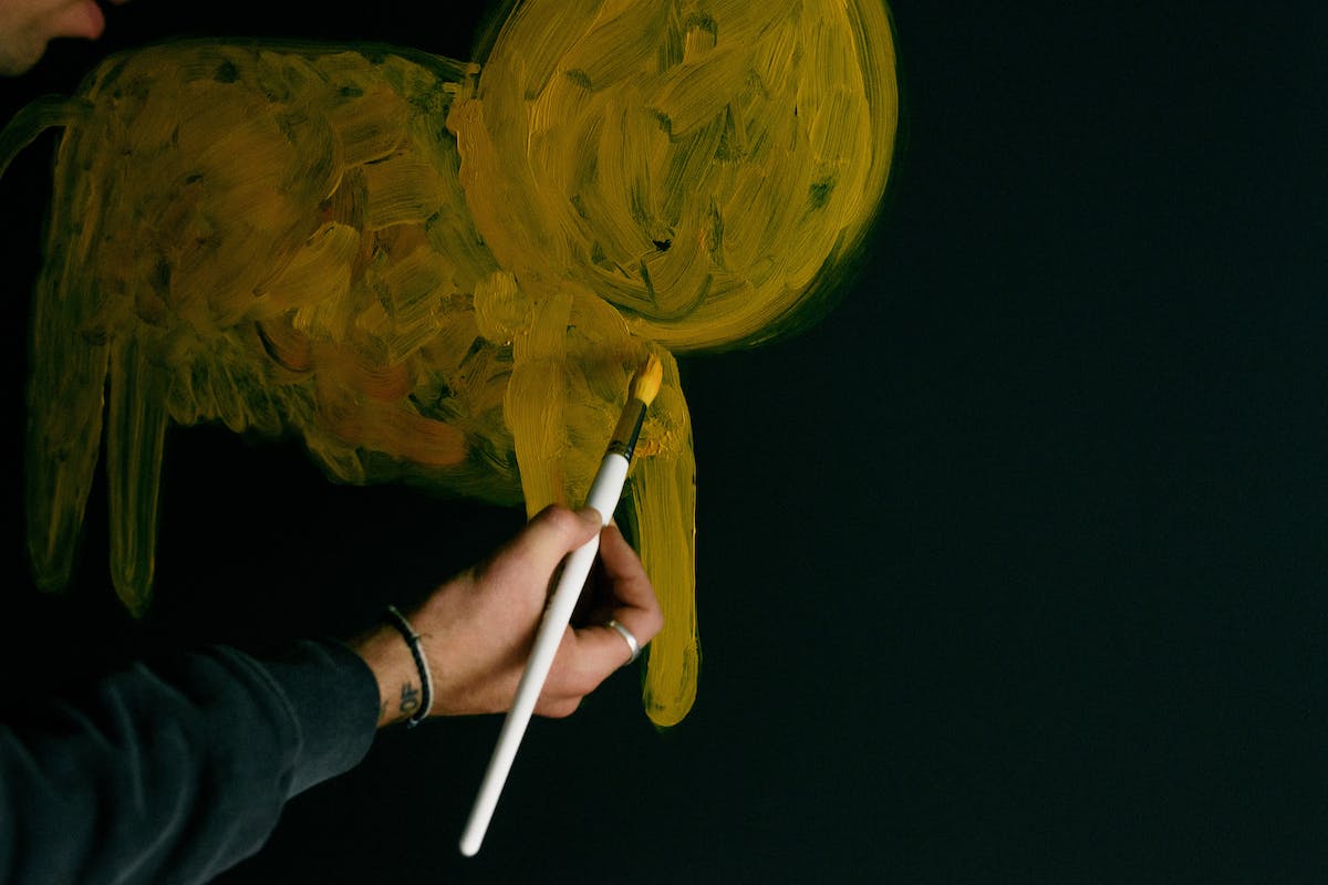 Uma pessoa pinta um fundo preto da parede com um pincel e tinta amarela