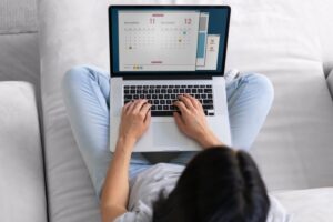 Uma mulher está com o notebook no colo conferindo o calendário 2024 com Feriados