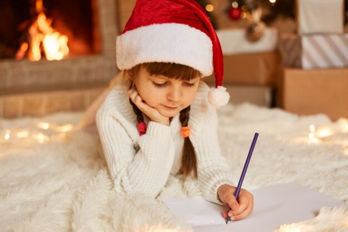 Uma menina está deitada de bruços no chão enquanto escreve um cartão de natal