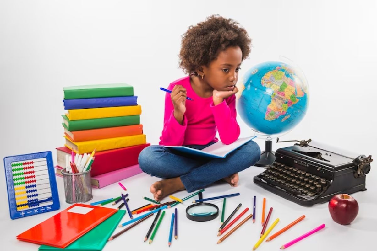 Uma aluna sentada em dúvida. Ao lado dela há um globo terrestre, pilha de caderno, uma máquina de escrever entre outros materiais