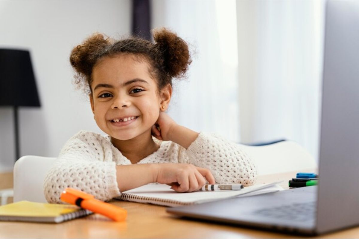 Uma aluna sorri para foto enquanto está sentada na frente de seu notebook