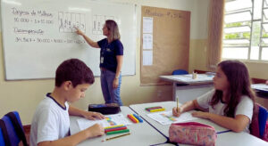 Dezena de milhar: Guia com QVL e atividades 4º e 5º ano (PDF) Professora explicando dezena de milhar no quadro para alunos.
